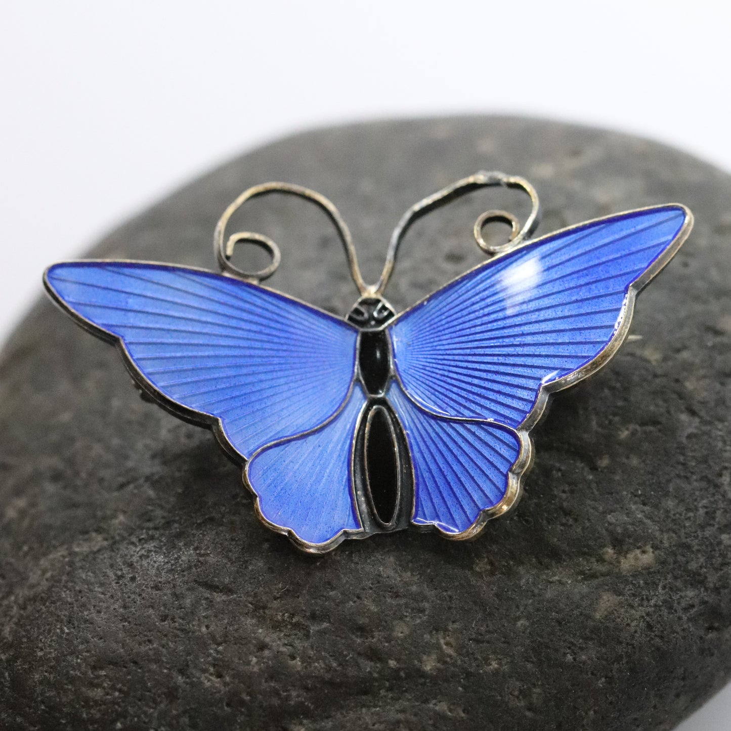 David Andersen enamel butterfly brooch in electric blue on a dark stone background