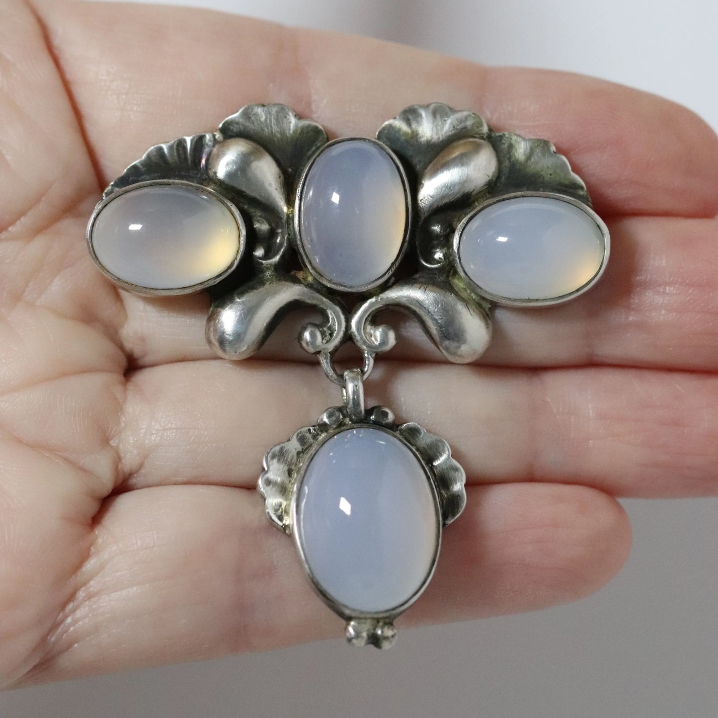 Hand holding a Georg Jensen moonstone sterling silver brooch with ornate floral design.