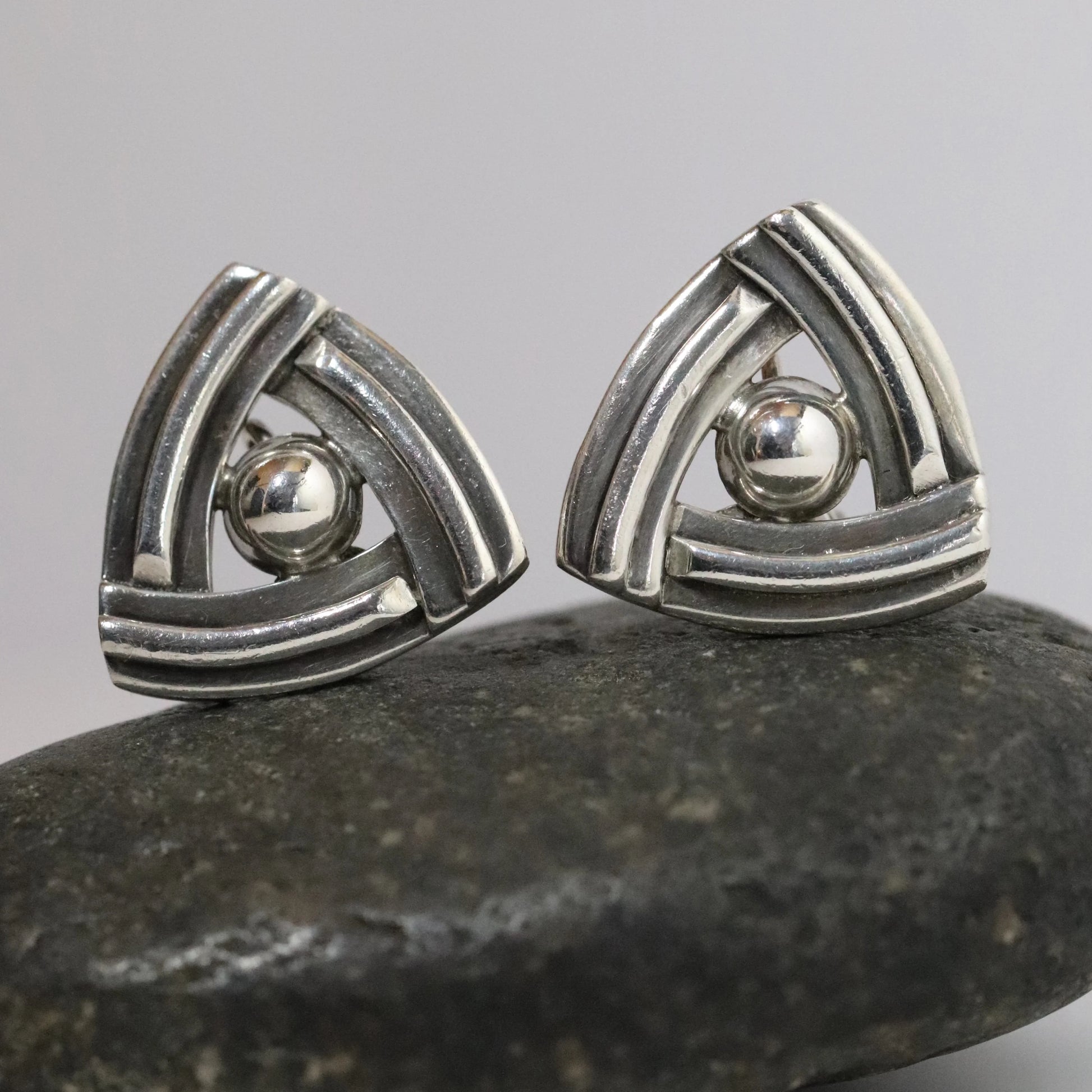 Geometric silver stud earrings with triangular design on stone surface