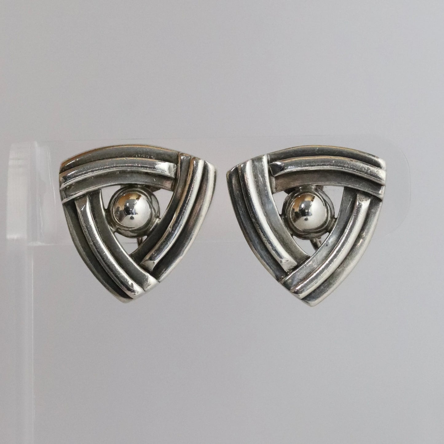 Geometric silver triangle earrings with central sphere on clear display, modern jewelry