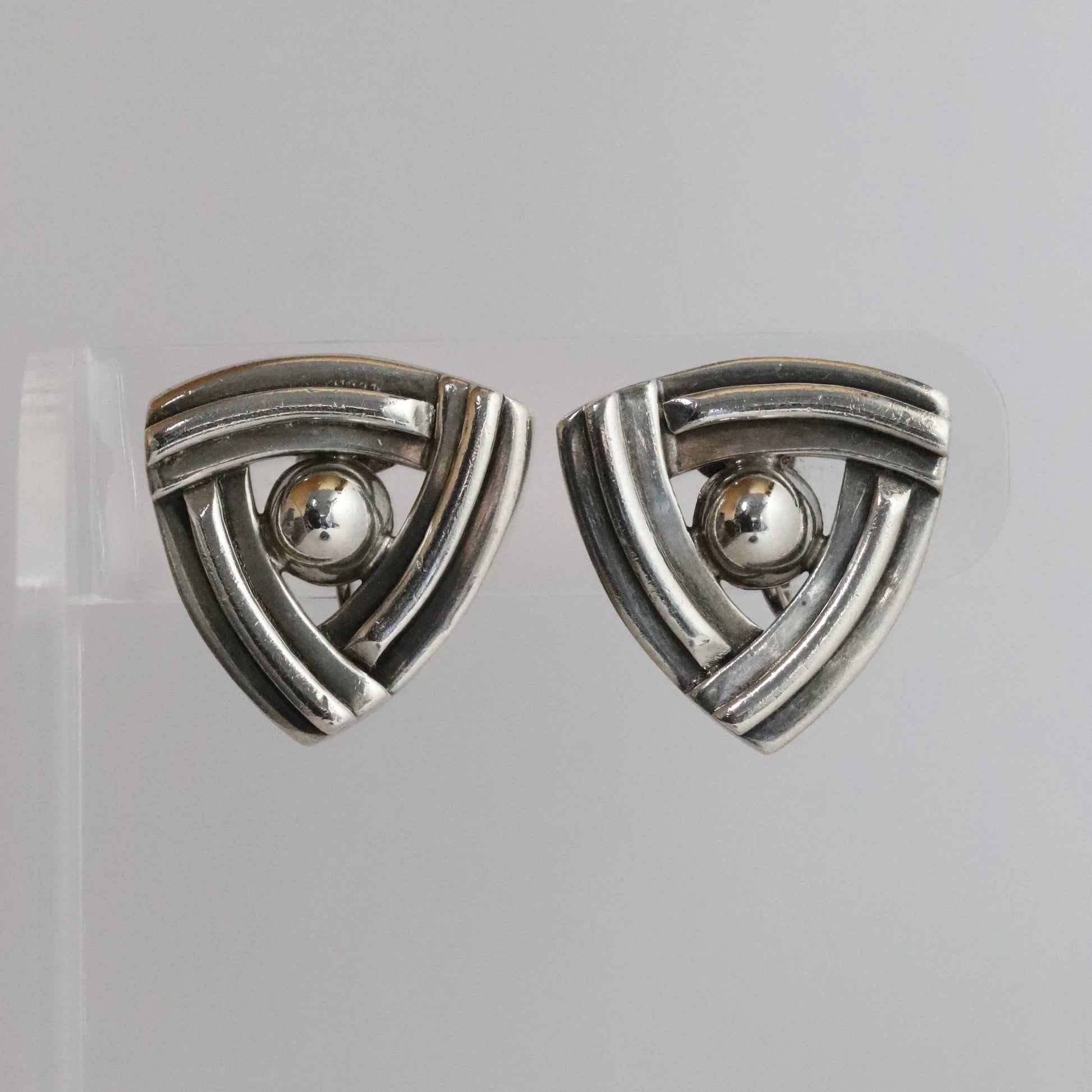 Geometric silver triangle earrings with central sphere on clear display, modern jewelry